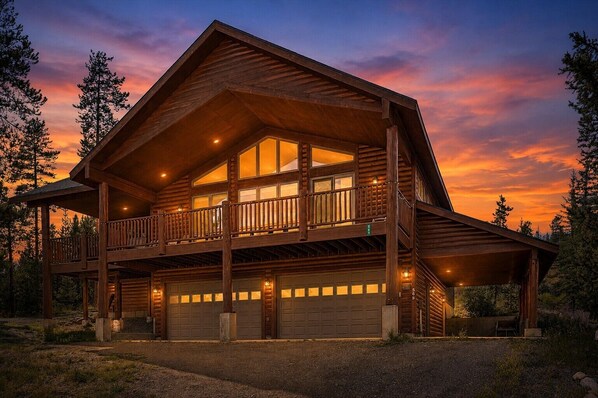 A two-story log cabin with a balcony, multiple garage doors, and a driveway.