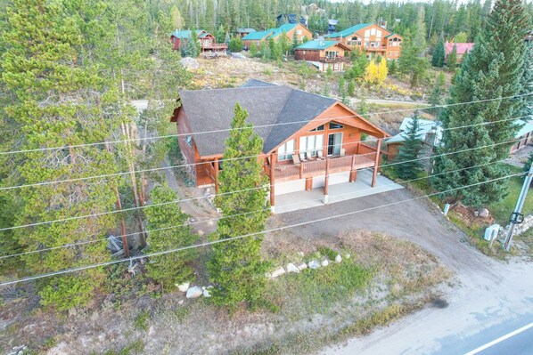 A wooden cabin with a porch, surrounded by dense forest and other cabins.