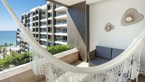 En balkon med hvid hængekøje, grå sofa og udsigt til en moderne bygning og havet.
