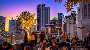 A rooftop bar with outdoor seating, city skyline views, and illuminated trees.
