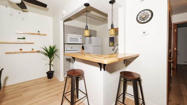 A kitchen with a wooden island, two stools, a ceiling fan, and a clock on the wall. - Groundfloor Modern Industrial 2BD Apartment (Anchorage)