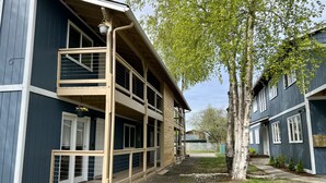 A two-story building with a balcony, a tree in front, and a clear sky. - Groundfloor Modern Industrial 2BD Apartment (Anchorage)