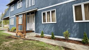 A two-story house with a porch, a front door, and a small garden area with plants. - Groundfloor Modern Industrial 2BD Apartment (Anchorage)