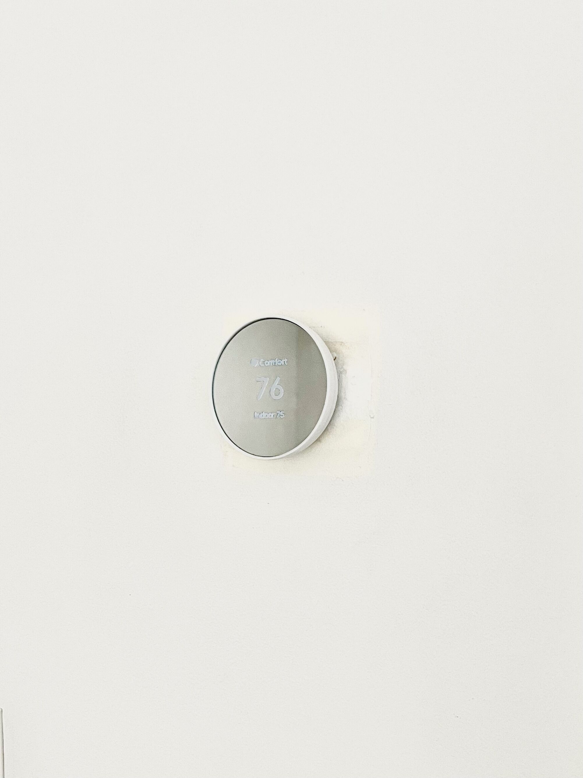 A thermostat with the brand 'Comfort' and model 'Indigo 75' on a white wall.