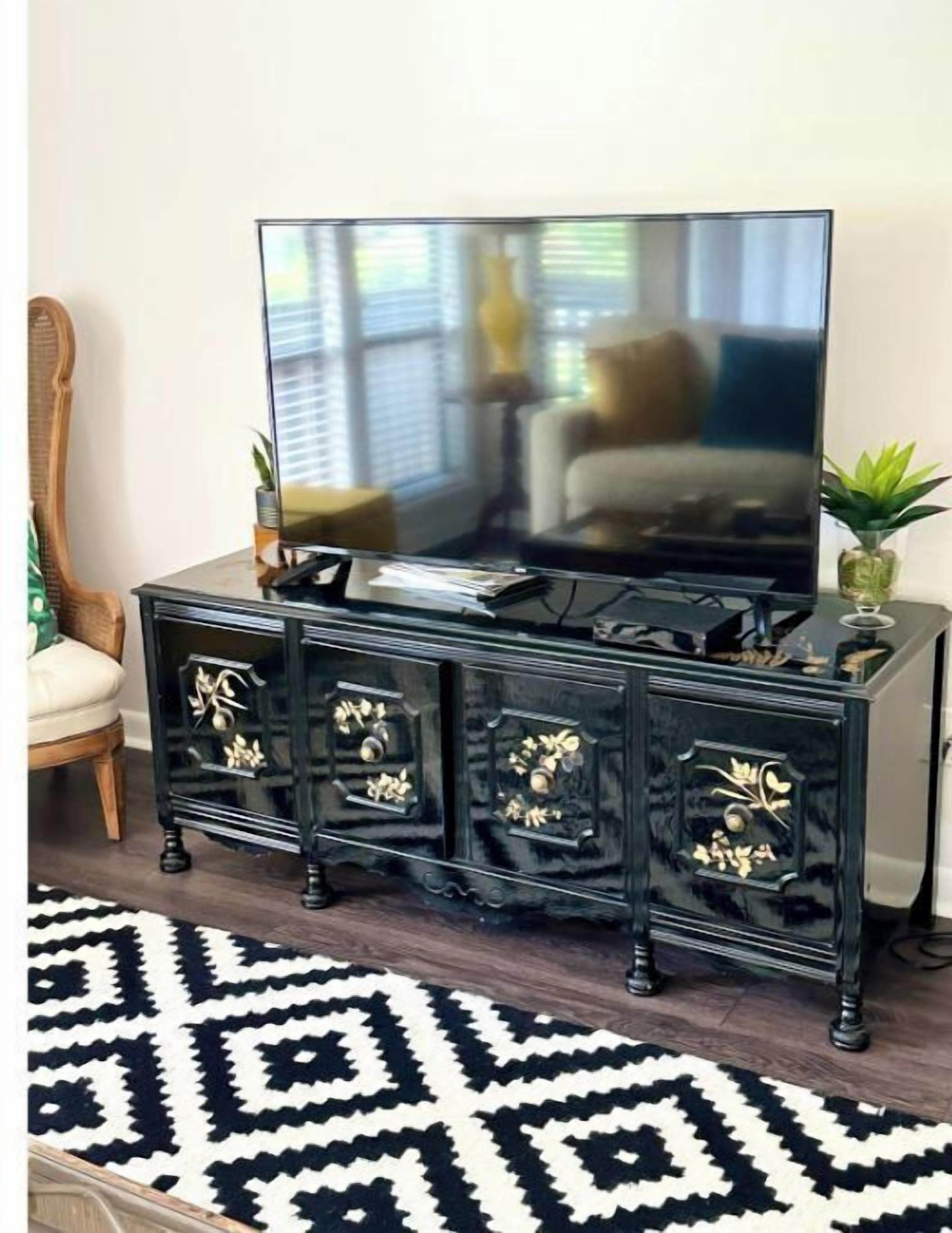 Een zwarte entertainmentkast met een flatscreen televisie, decoratieve kastdeurtjes en een kamerbreed tapijt met een patroon.