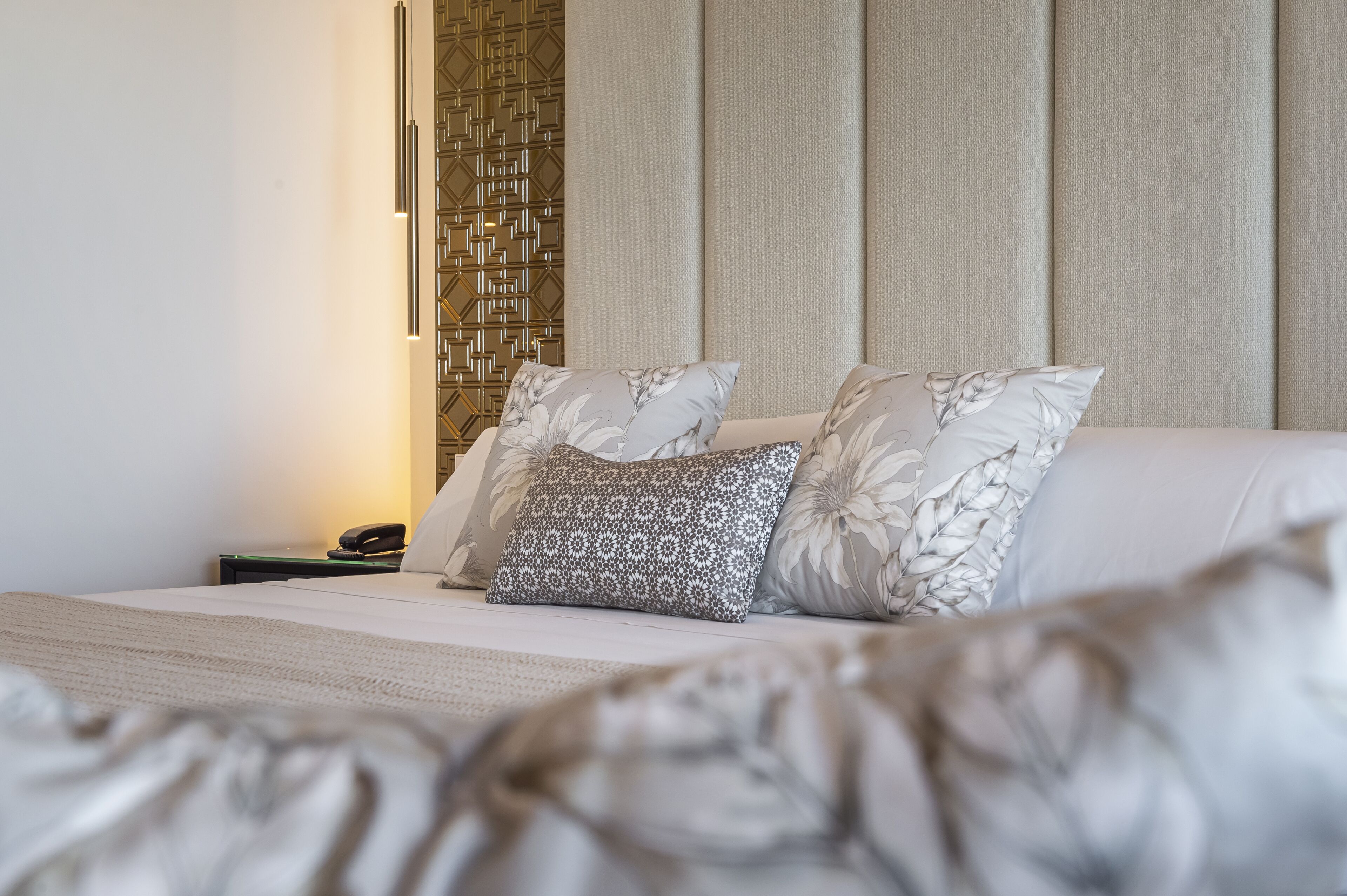 Un dormitorio ordenado con cama, almohadas, mesita de noche y teléfono.