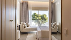 Habitación de hotel moderna con una cama grande, un sofá y un balcón con vistas a árboles.