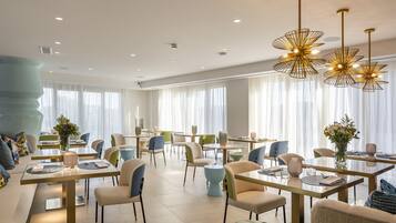 Un comedor moderno con mesas y sillas, ventanas amplias y lámparas decorativas.