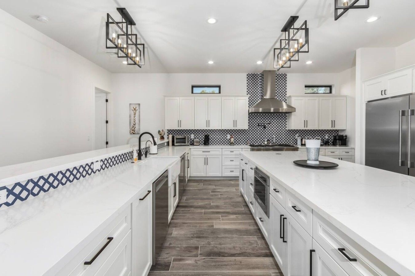 A modern kitchen with white cabinetry, a large island, and a stainless steel refrigerator.