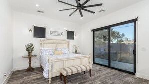 A bedroom with a bed, a bench, a small table with a plant, and a sliding glass door leading to an outdoor area. - Arcadia/Scottsdale 4bedroom/4.5bath Camelback Mountain New Build-Prime Location (Phoenix)