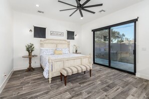 A bedroom with a bed, a bench, a small table with a plant, and a sliding glass door leading to an outdoor area.