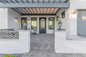 A covered patio area with a wooden pergola, white brick walls, and a black door.