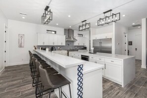 A modern kitchen with a central island, bar stools, and a stainless steel refrigerator.