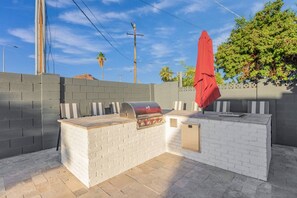 An outdoor barbecue area with a grill, seating, and a red umbrella.