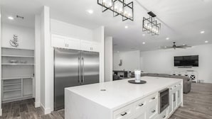 Una cocina moderna con armarios blancos, una isla grande, electrodomésticos de acero inoxidable y un ventilador de techo.