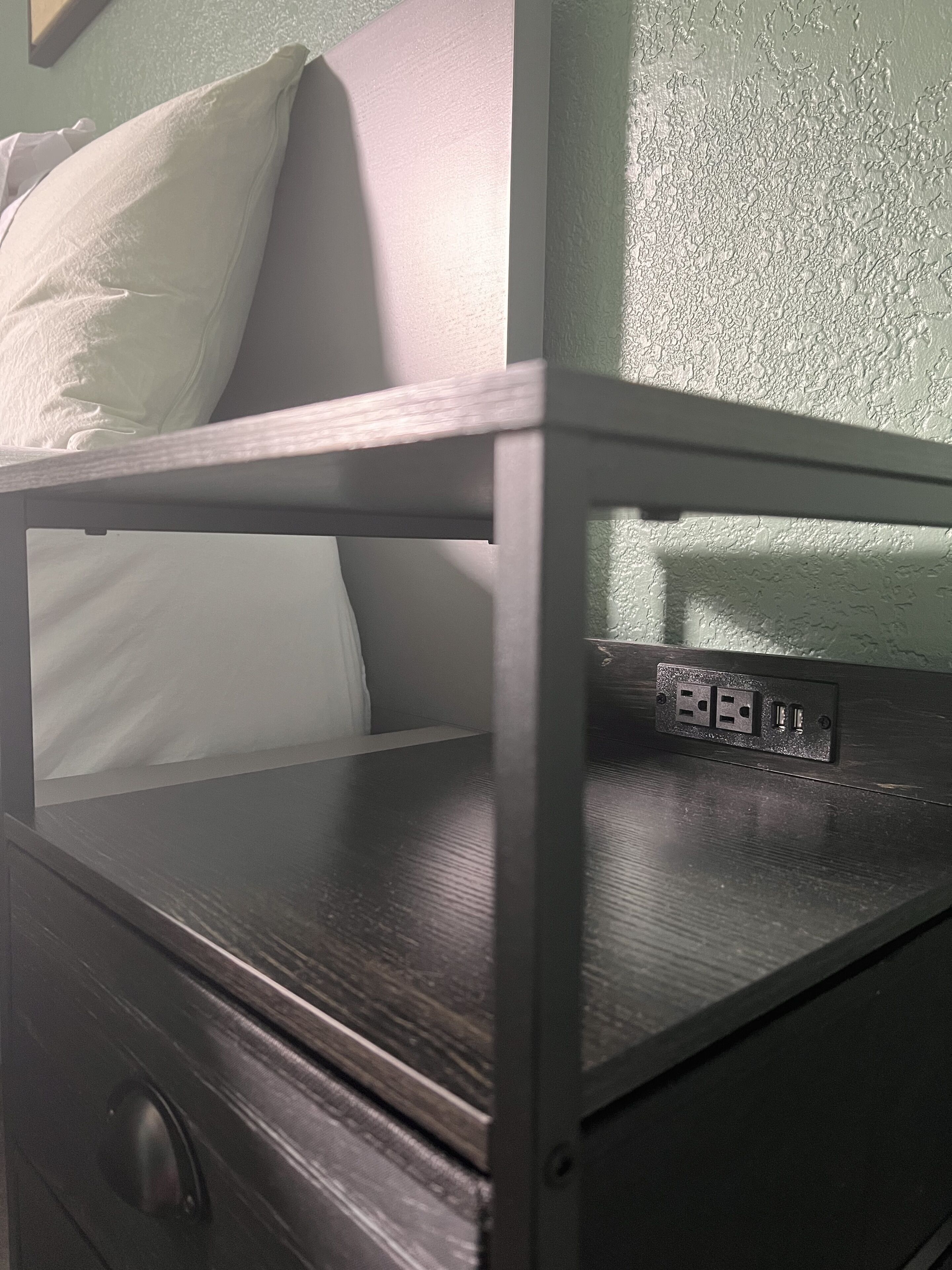 Un lit superposé avec une tête de lit, une table de chevet et une prise de courant.