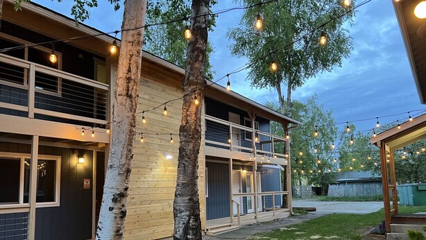 A two-story building with a balcony, string lights, and a tree in the foreground. - Delightful Sleek Modern 2 Bed 1 Bath apt (Anchorage)
