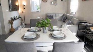 A modern dining area with a white table set for four, surrounded by grey chairs. A potted plant adds a touch of greenery. - Villa Lota with a heated pool, sauna & E-car charger (Sveti Ivan Dobrinjski (Krk))