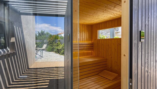 A sauna with wooden benches and a window, leading to an outdoor area with a patio and chairs. - Villa Lota with a heated pool, sauna & E-car charger (Sveti Ivan Dobrinjski (Krk))