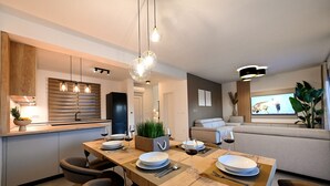 A modern kitchen with a wooden dining table set for four, a built-in oven, and a large flat-screen TV in the living area. - Villa Nostro Porto with heated pool (Kožino)