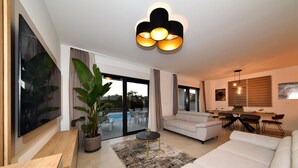 A modern living room with a large flat-screen TV, a sofa, a dining area, and a large window with curtains. - Villa Nostro Porto with heated pool (Kožino)