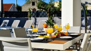 An outdoor dining area with a table set for two, featuring a fruit bowl, plates, cutlery, and glasses of orange juice. - Villa Nostro Porto with heated pool (Kožino)