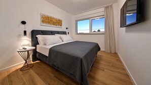 A modern bedroom with a bed, a side table, a wall-mounted TV, and a large window with curtains. - Villa Nostro Porto with heated pool (Kožino)