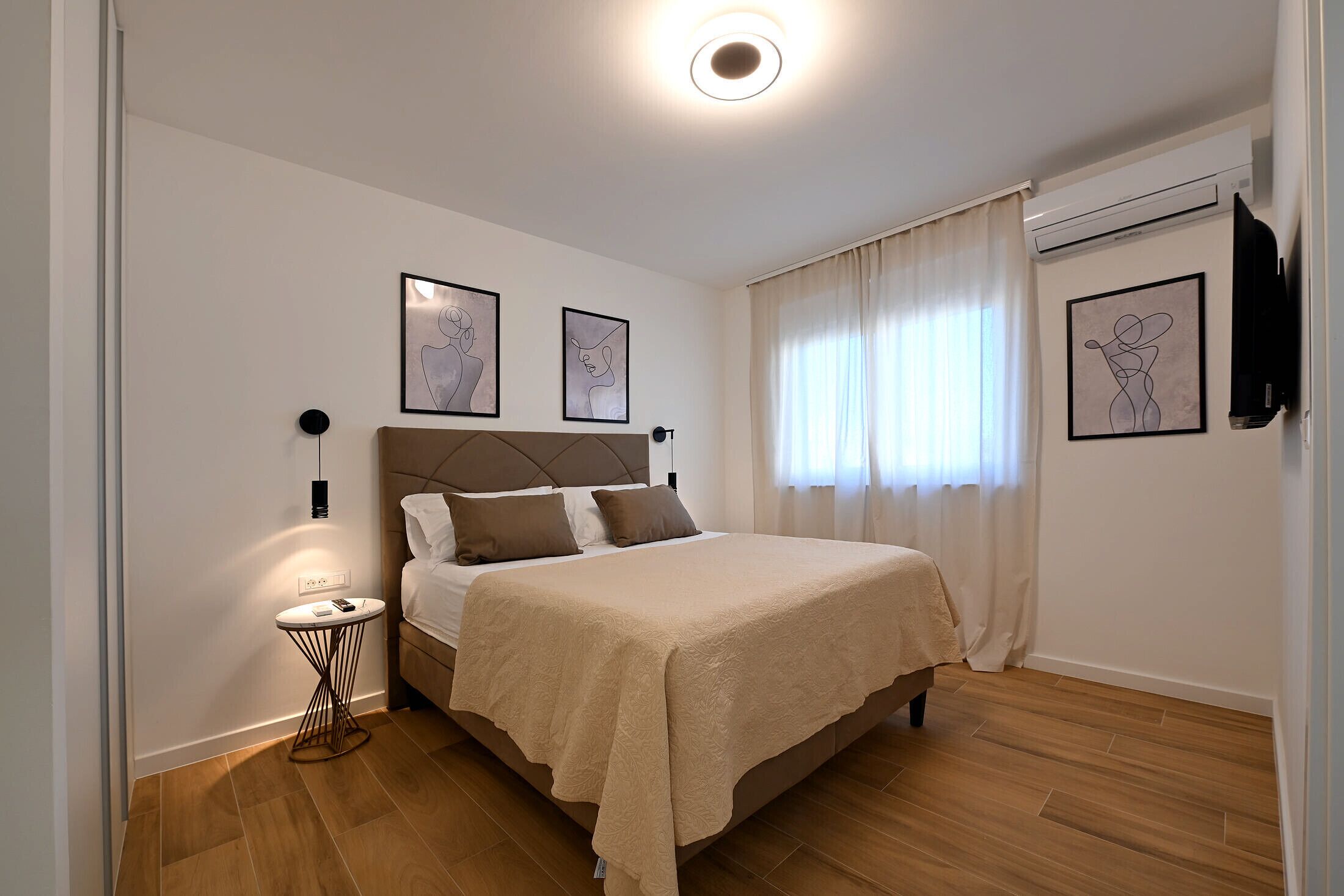 A bedroom with a bed, a bedside table, a wall-mounted TV, and artwork.