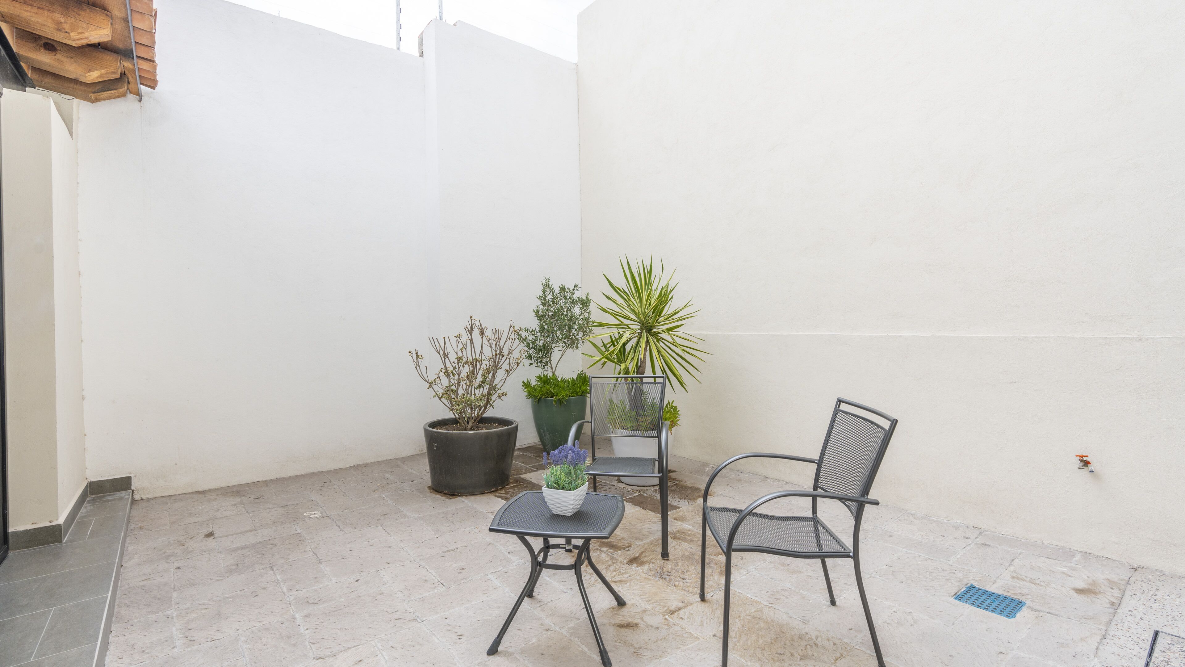 A small patio area with a table and two chairs, surrounded by potted plants.