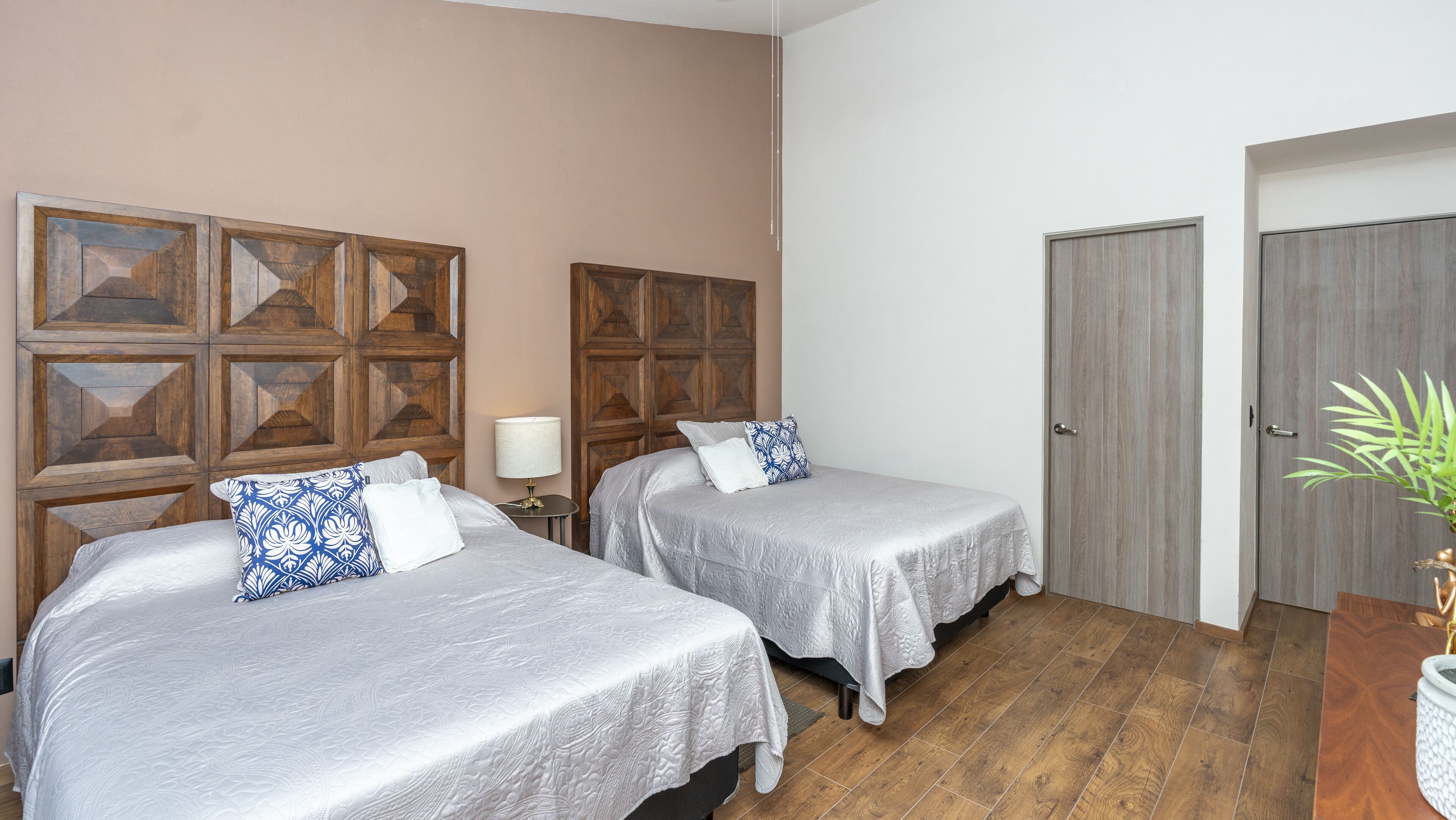 Ein Zimmer mit zwei Betten, Holzkopfenden, einer Holztür und einem Blumentopf.