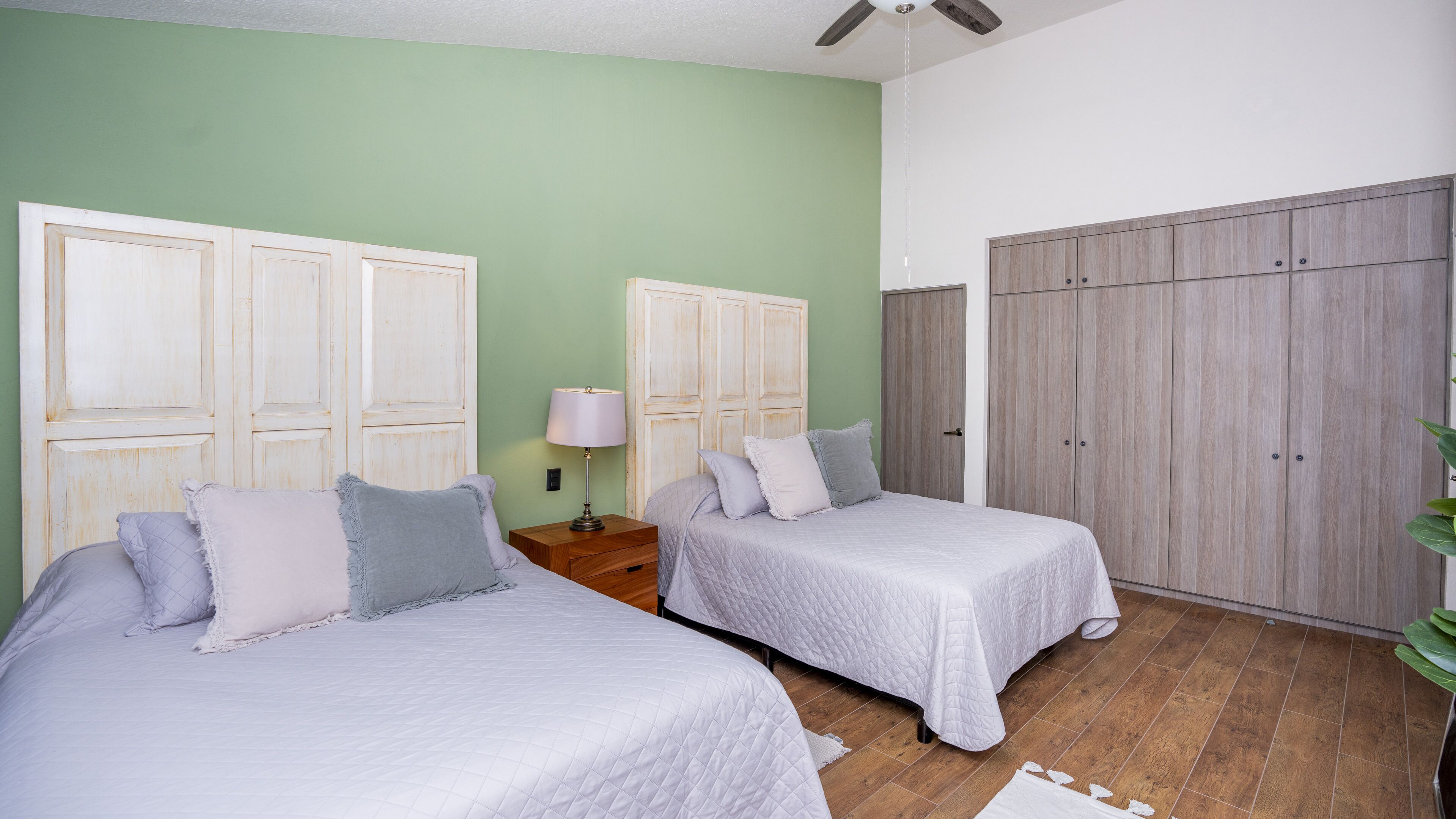 A bedroom with two beds, a nightstand, a lamp, and wardrobes.