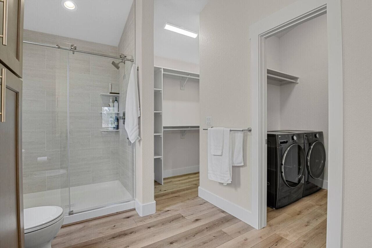 A modern bathroom with a glass shower enclosure, a toilet, and a built-in washing machine.