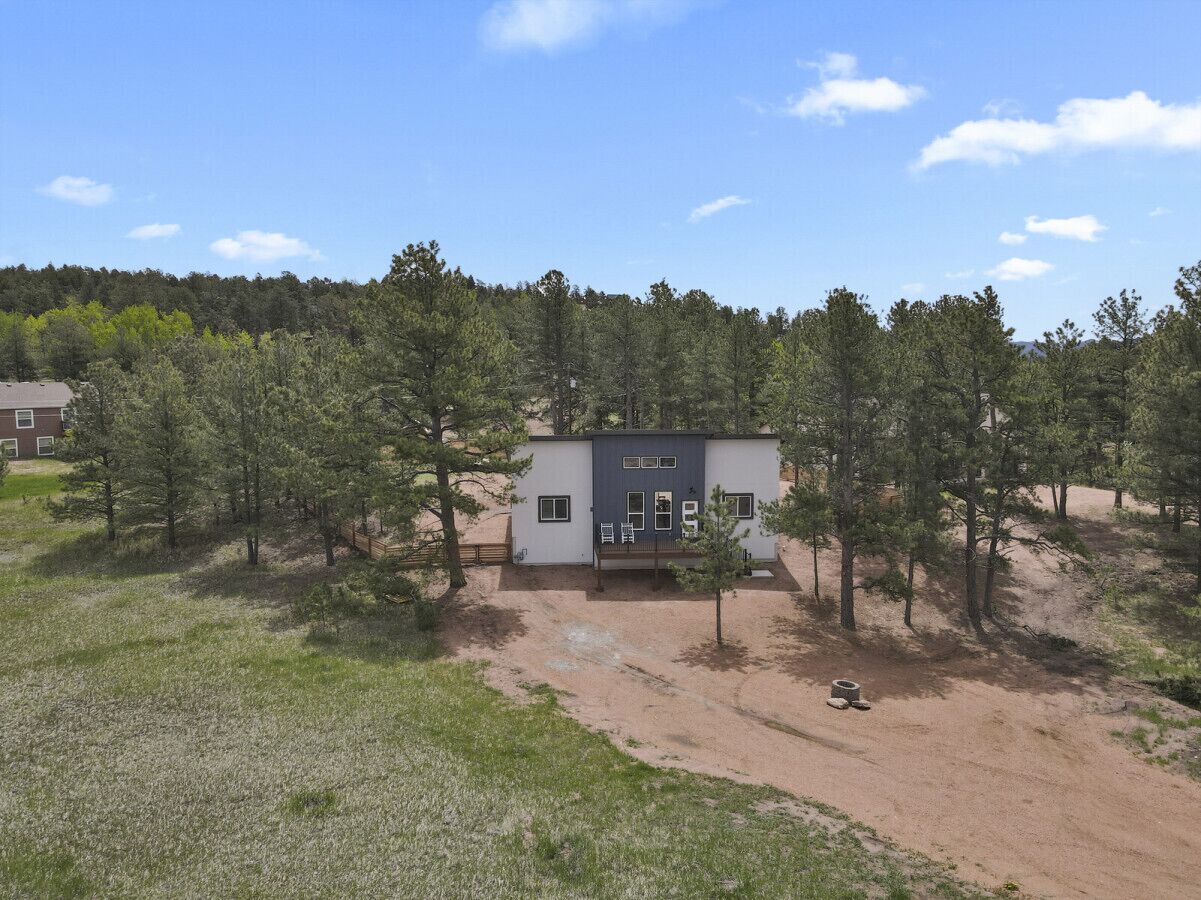 A modern building with a flat roof, surrounded by trees and a dirt path.