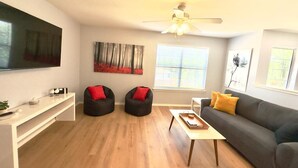 A modern living room with a flat-screen TV, two bean bags, a grey sofa with yellow pillows, a wooden coffee table, and artwork on the walls. - #Rental Welcomes #Nurses #Sea World #JBSA #Medical Center #USAF #ARMY #BMT #NSCA (San Antonio)