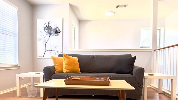 A living room with a dark grey sofa, a white coffee table, and a yellow pillow. There is a framed artwork on the wall and a window with blinds. - #Rental Welcomes #Nurses #Sea World #JBSA #Medical Center #USAF #ARMY #BMT #NSCA (San Antonio)