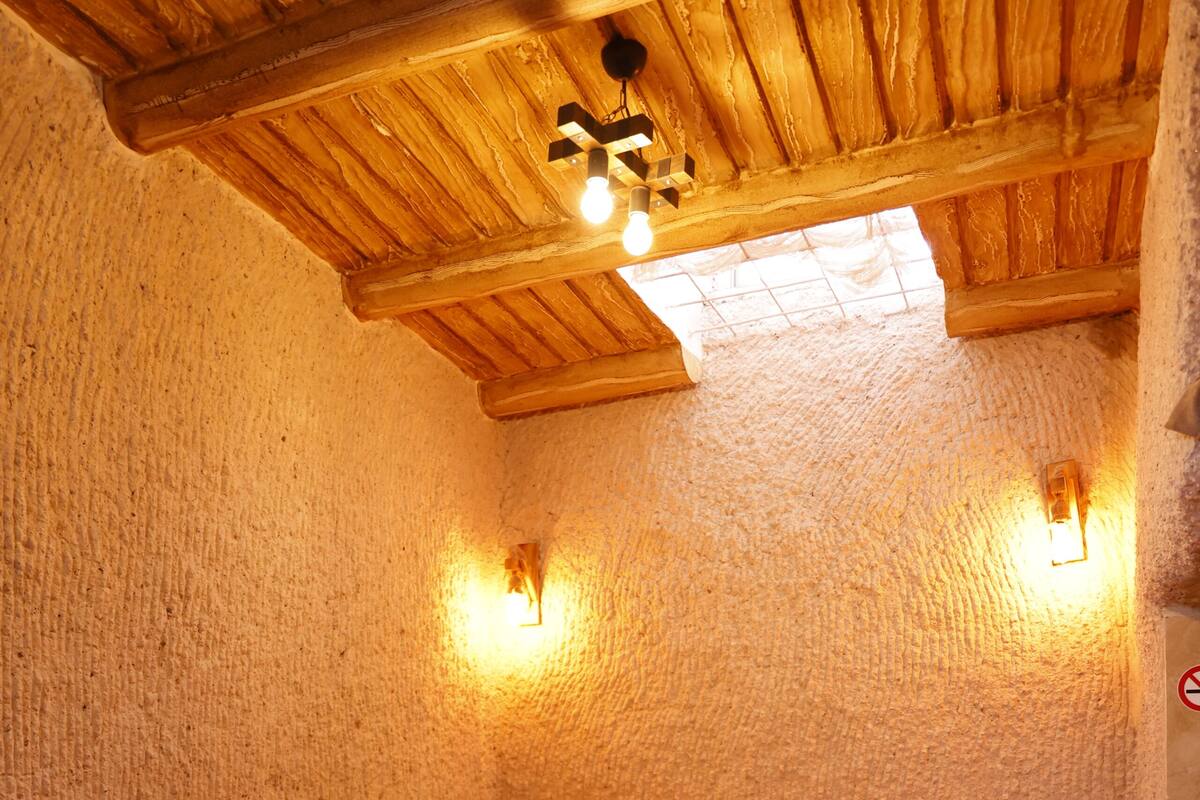 A bedroom with a wooden ceiling, a bed with a floral bedspread, and two wall-mounted lights.