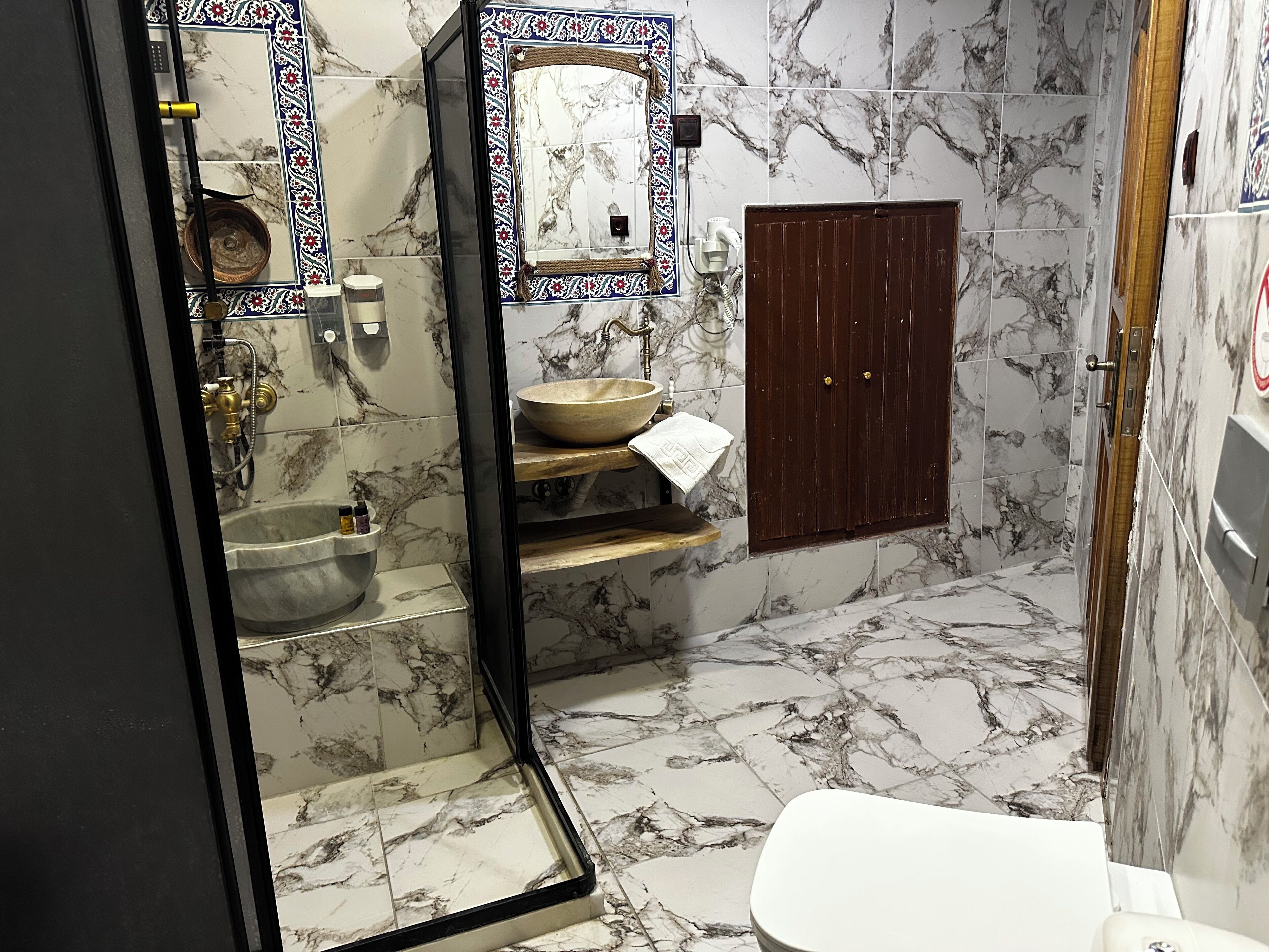 A bathroom with a marble floor, a sink, a mirror, and a wooden cabinet.