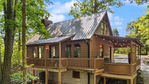 Une cabane en bois dotée d’une terrasse, de grandes fenêtres et d’une cheminée.