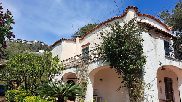 Um edifício branco com telhado de telhas vermelhas, portas em arco e uma varanda com grades de ferro forjado.