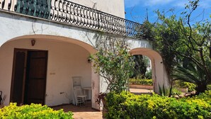 Um edifício com varanda, porta em arco e um pequeno pátio com mesa e cadeiras.