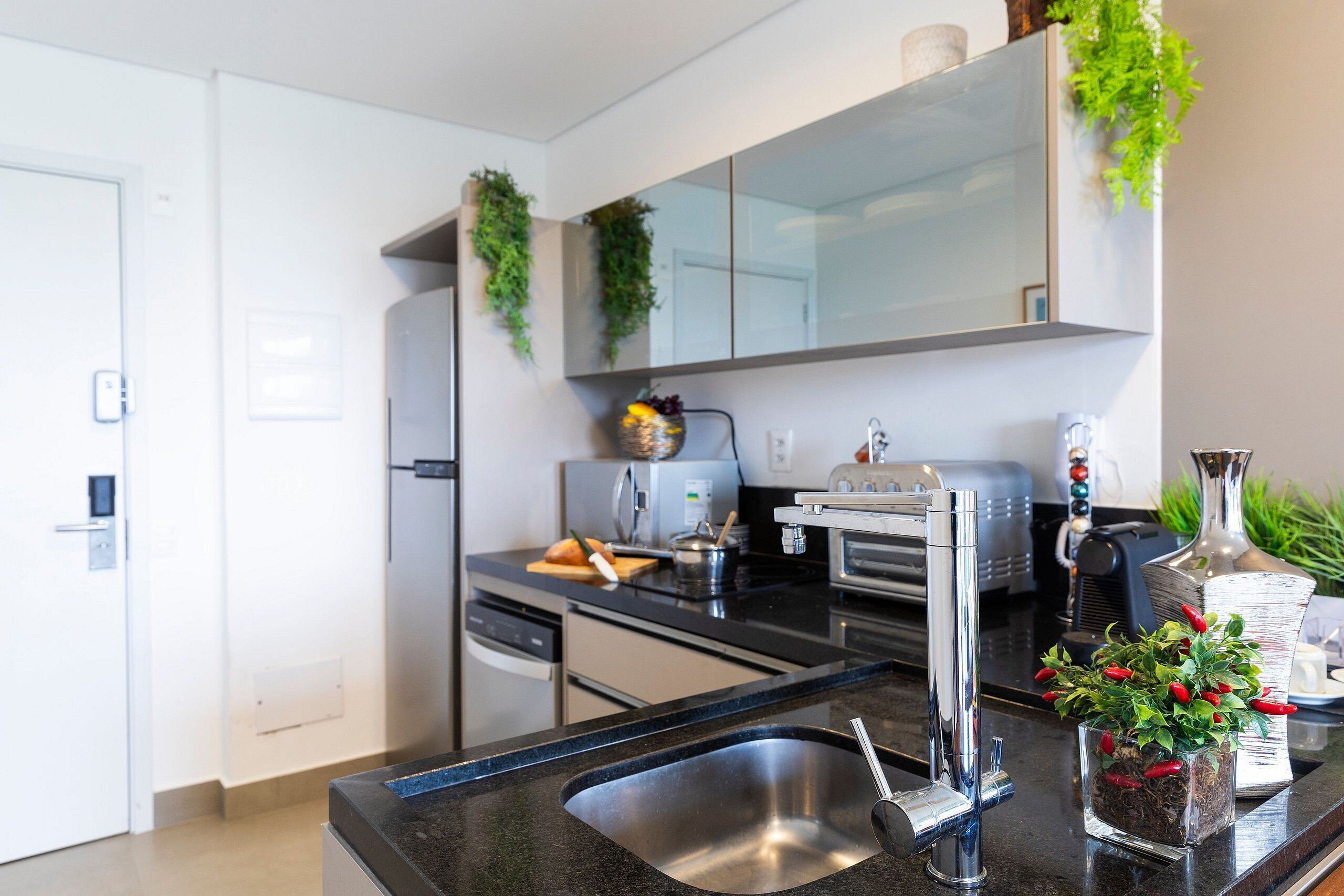 Et moderne køkken med rustfrie hårde hvidevarer, en sort bordplade og en lille potteplante.