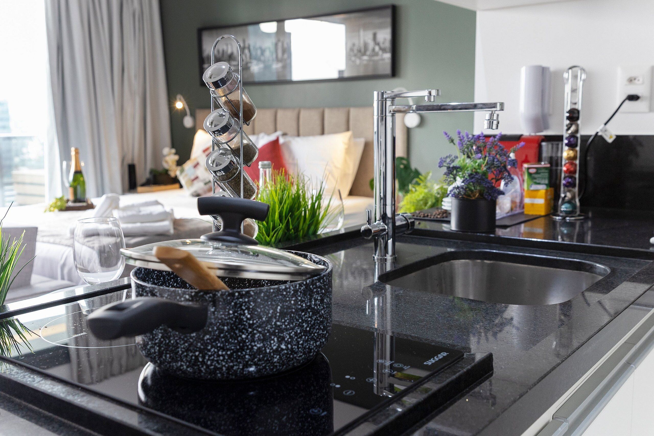 A modern kitchen with a glass cooktop, stainless steel sink, and a dining area with a sofa and decorative plants.