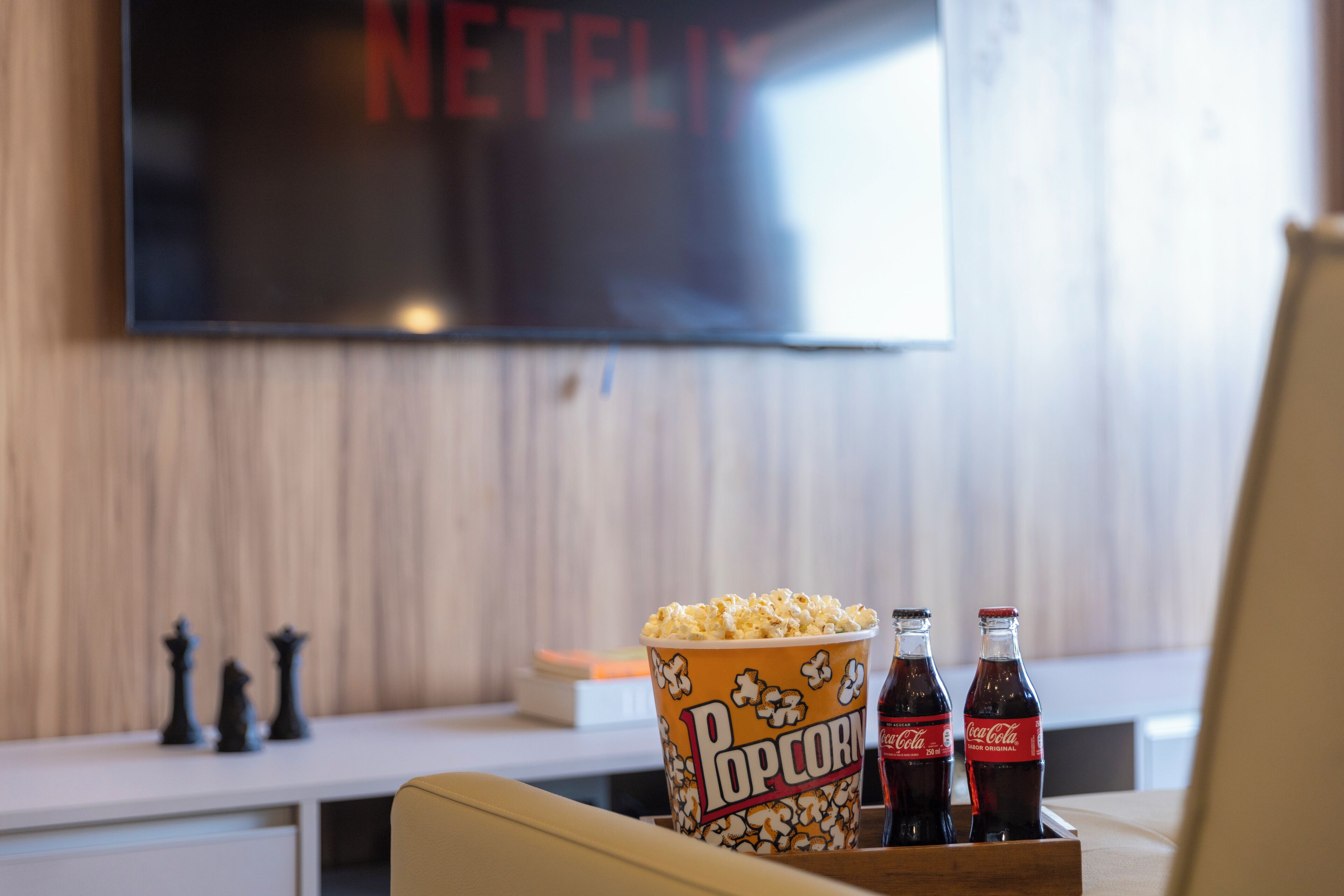 En hyggelig stue med et stort fladskærms-tv, en popcorn-spand og to Coca-Cola flasker.