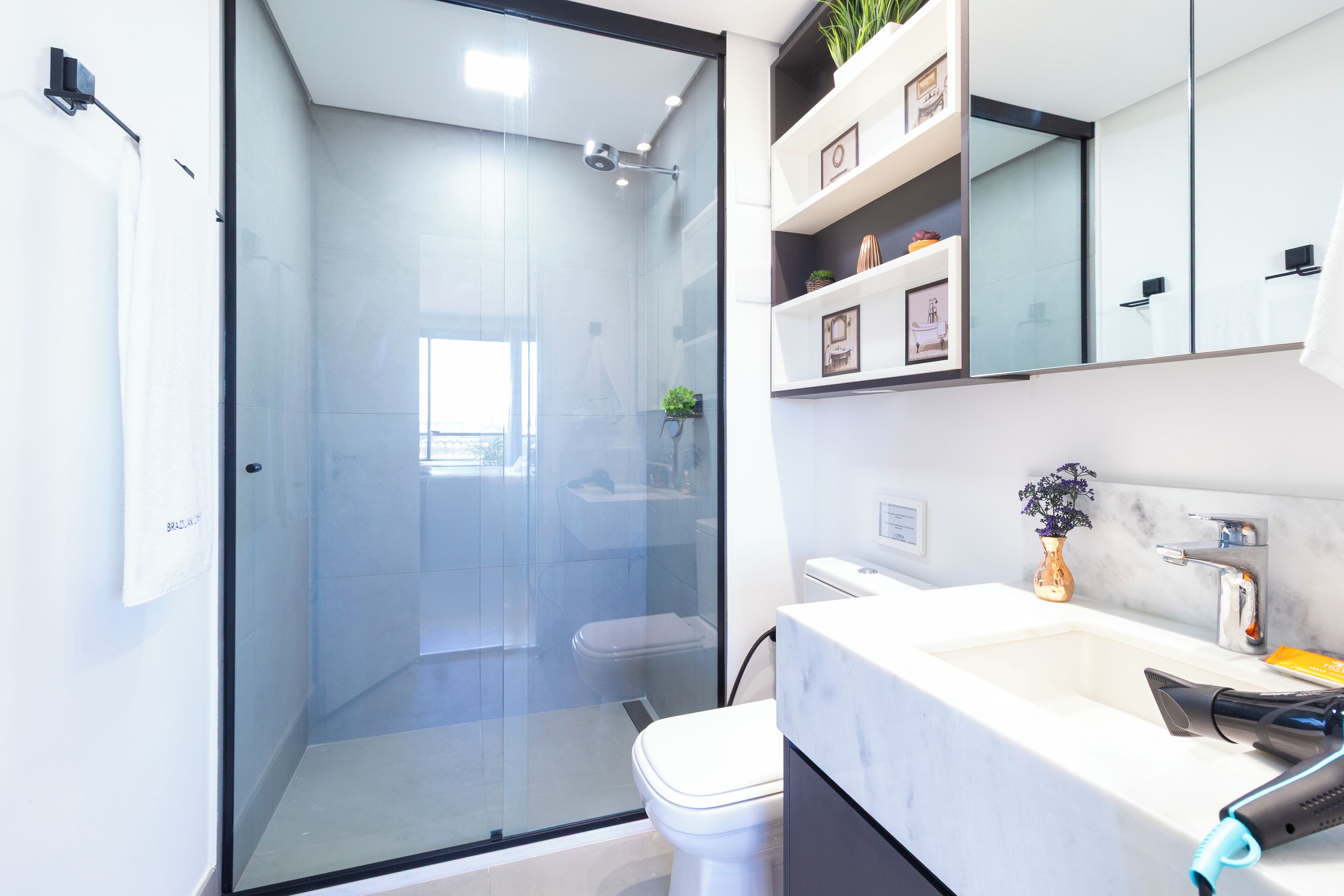 A modern bathroom with a glass-enclosed shower, a white sink with a marble countertop, and a mirror above the sink.