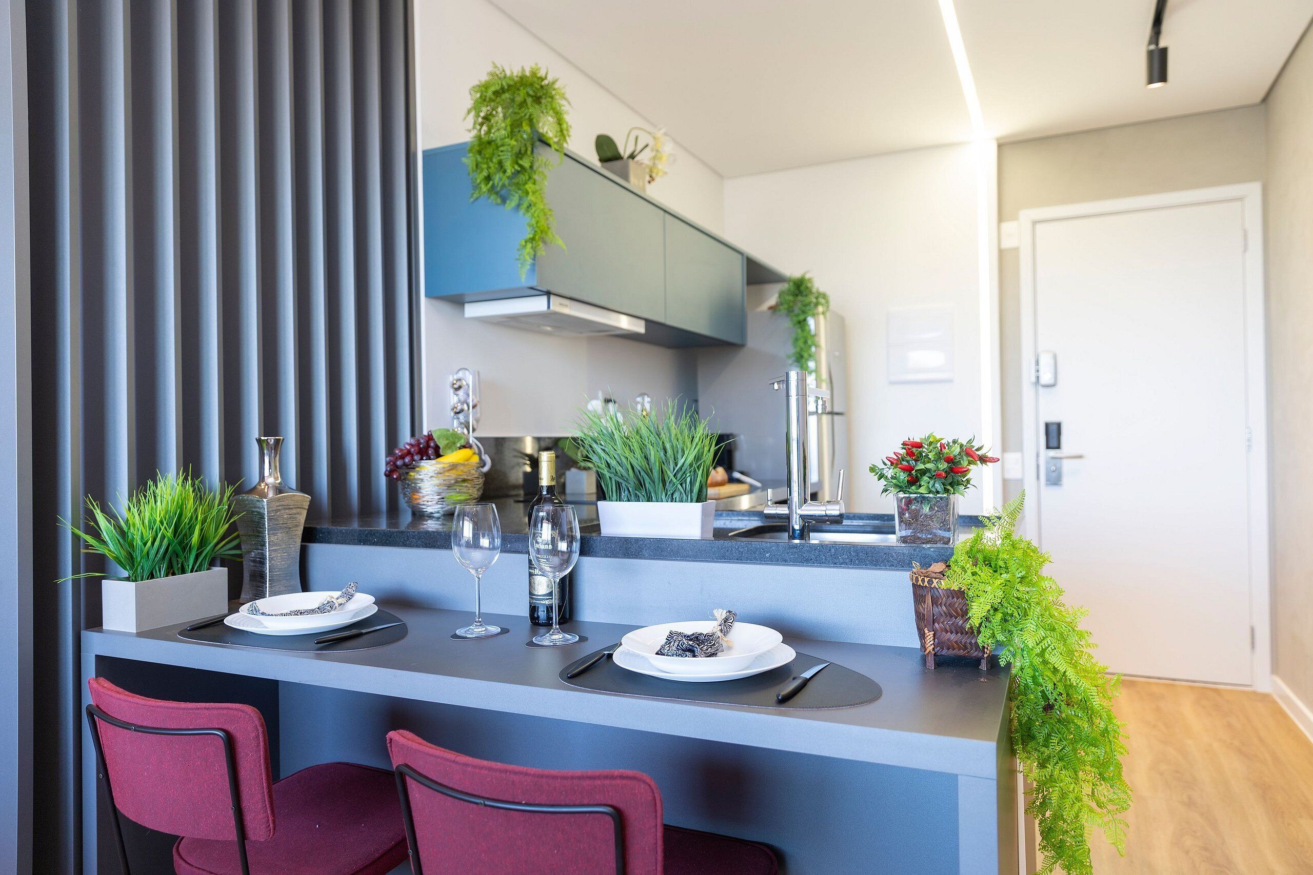 A modern kitchen with a central island, bar stools, and potted plants.
