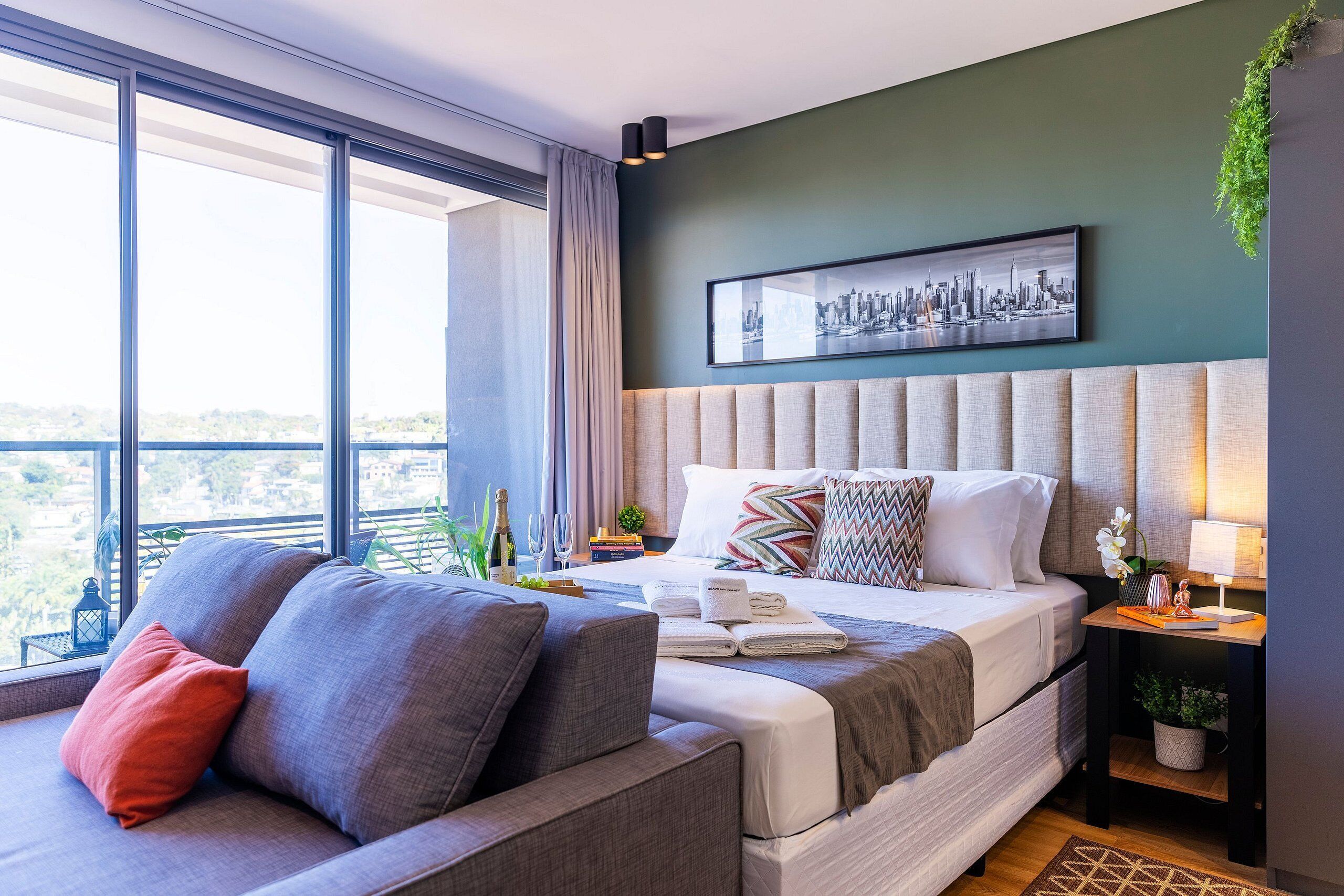 Una habitación de hotel moderna con una cama grande, un sofá y vistas a la ciudad a través de amplias ventanas.