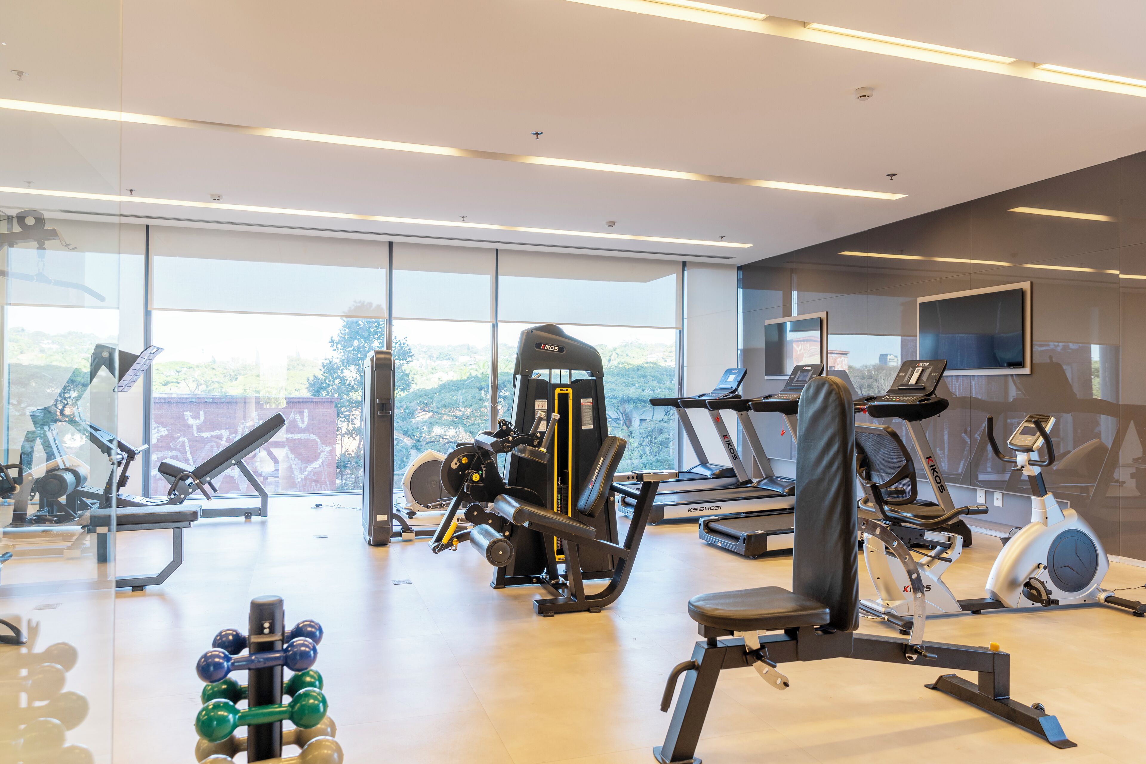 Un gimnasio con equipos de ejercicio variados, amplias ventanas y un diseño moderno.