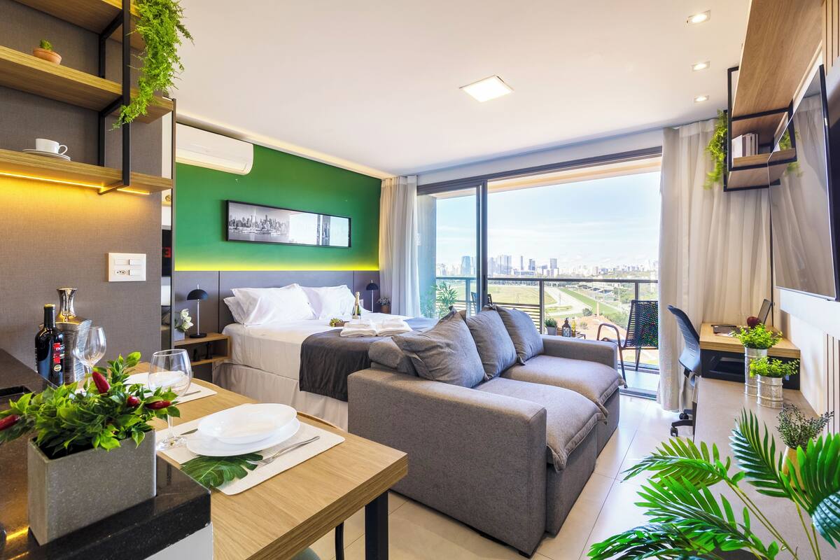 Ein modernes Hotelzimmer mit Bett, einer Couch, einem Esstisch und Blick auf die Stadt.