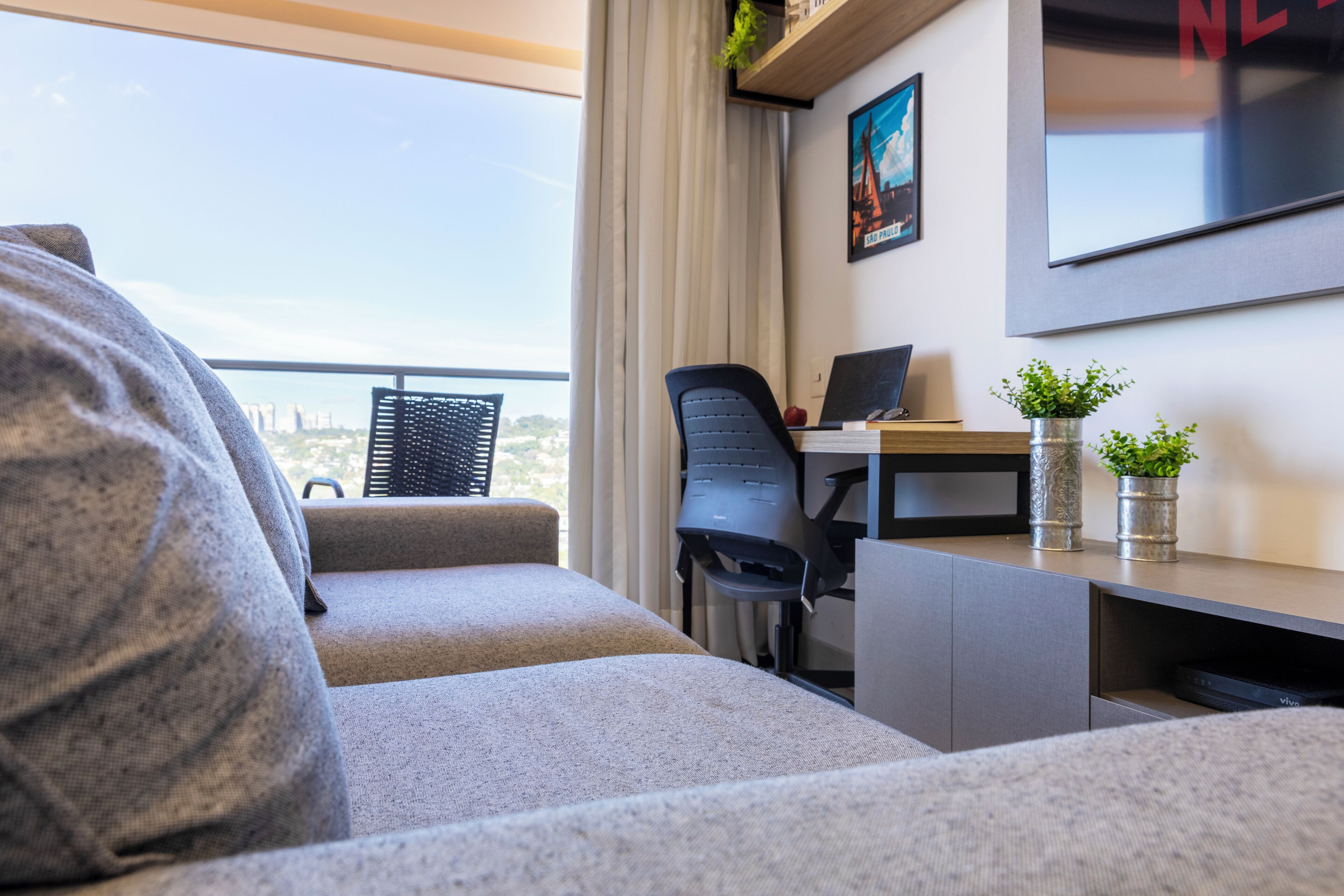 Et moderne hotelværelse med sofa, skrivebord med en bærbar computer og udsigt over byen.