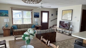 Uma sala de estar com uma mesa de jantar de madeira, um sofá, uma televisão e uma escada.